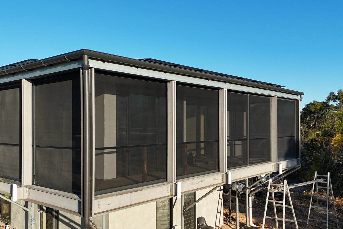 Corner of a new Agnes Water home with dark mesh screens enclosing the upper deck